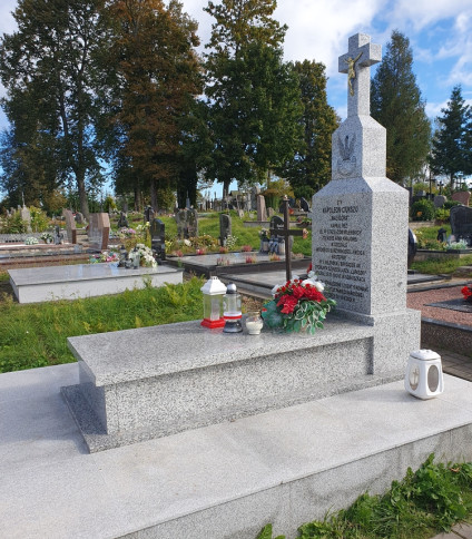 Grób żołnierza Armii Krajowej Apoloniusza Ciukszy z drewnianym krzyżem i metalową tabliczką. Otoczony kwiatami i zniczami na cmentarzu w Powiewiórce.