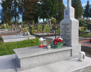 Grób żołnierza Armii Krajowej Apoloniusza Ciukszy z drewnianym krzyżem i metalową tabliczką. Otoczony kwiatami i zniczami na cmentarzu w Powiewiórce.