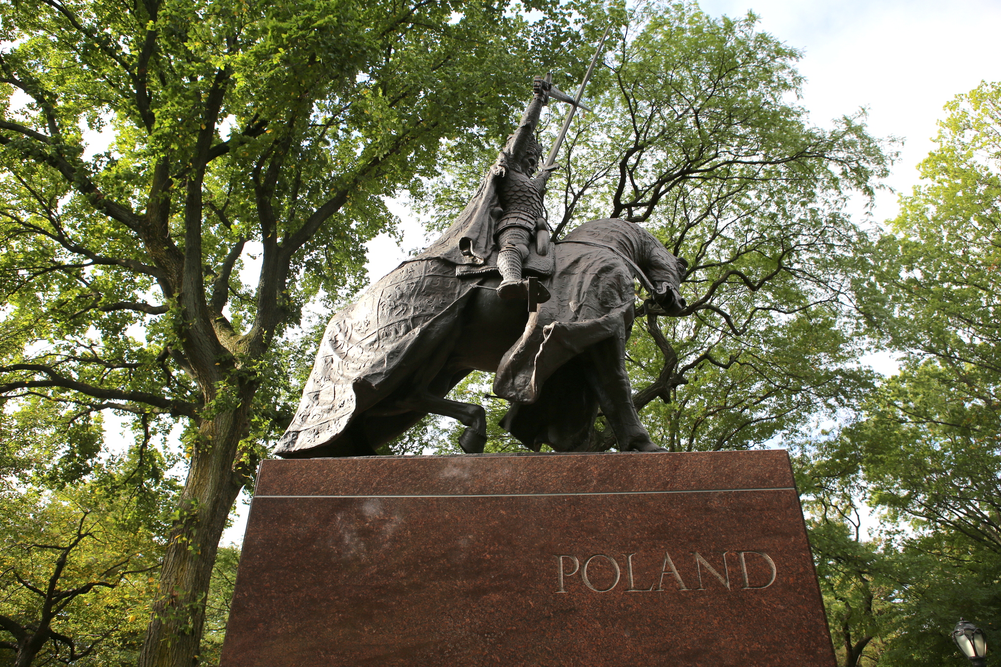 Equestrian statue of King Władysław II Jagiełło in Central Park, New York, with the word 'POLAND' on the pedestal. The statue is surrounded by trees.