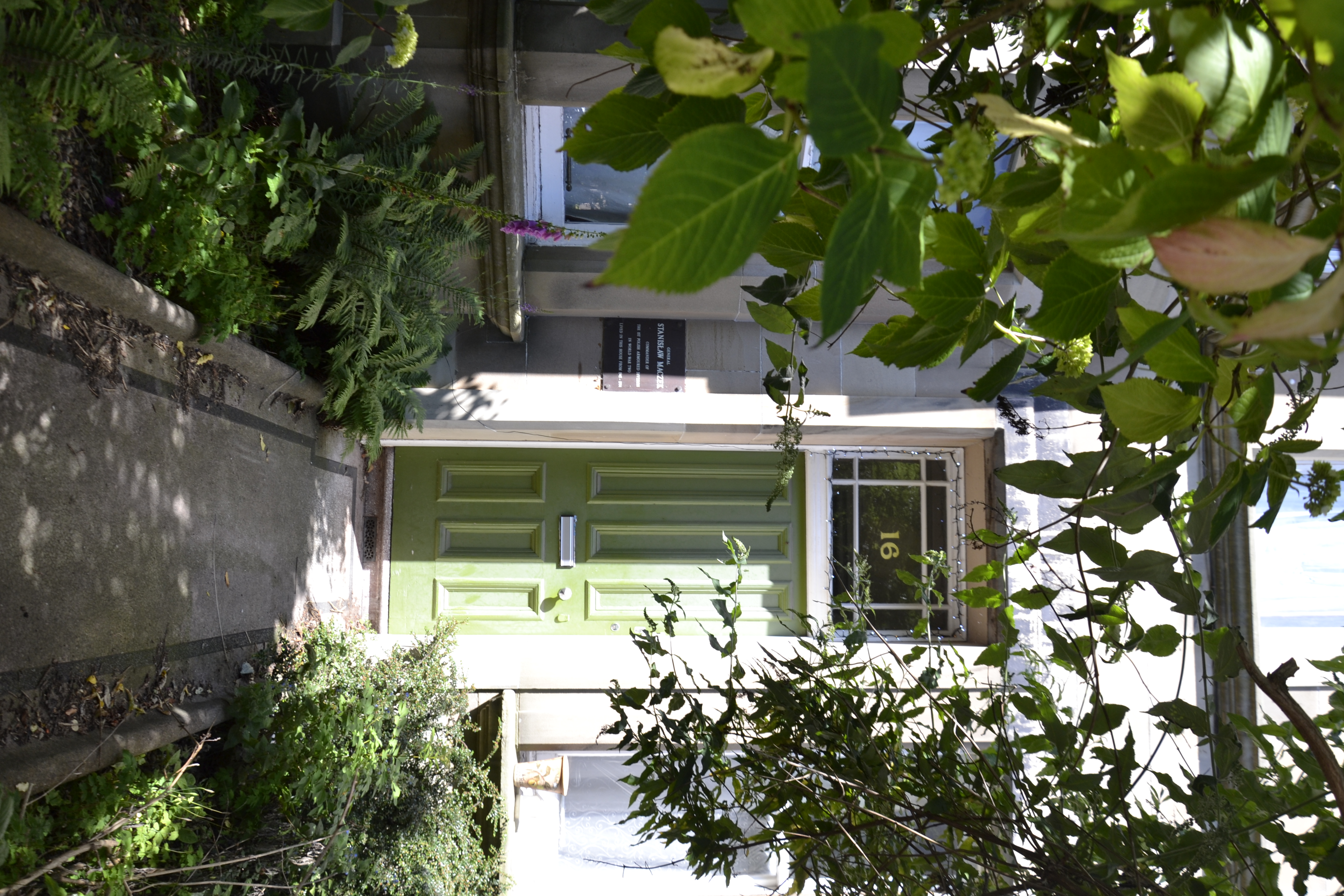 Les portes vertes de l'ancienne résidence de Stanislaw Maczek, au 16 Arden Street, à Édimbourg, entourées d'hortensias luxuriants et de verdure.