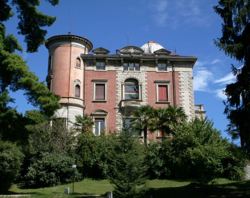 Willa Toeplitz w Varese, neorenesansowy budynek z okrągłą wieżą i kopułą obserwatorium, otoczony bujną zielenią i drzewami.