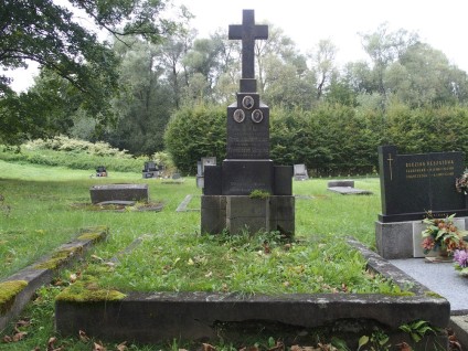 Grób oznaczony krzyżem z dwustopniowym cokołem i podstawą. Cokół z trzema medalionami z fotografiami i rytowanymi inskrypcjami. Przed nim żardiniera o nieregularnym kształcie.