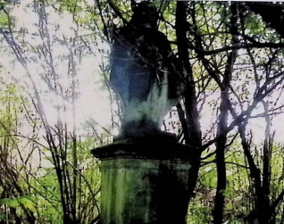 Grób oznaczony figurą Matki Boskiej na dwustopniowym cokole, otoczony drzewami. Matka Boska ma rozpuszczone włosy, szatę spiętą na przeponie i płaszcz. Ręce rozłożone w geście przygarnięcia.