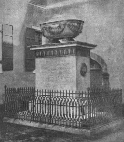 Pomnik generała Paca w Smirnie, z białym marmurowym sarkofagiem na cokole, otoczony żelaznym ogrodzeniem. Pomnik znajduje się na dziedzińcu z budynkiem w tle.