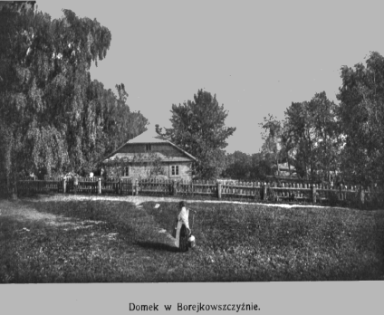 Drewniany domek w Borejkowszczyźnie otoczony drzewami i drewnianym płotem. Na pierwszym planie osoba z wiadrem idzie po trawie.