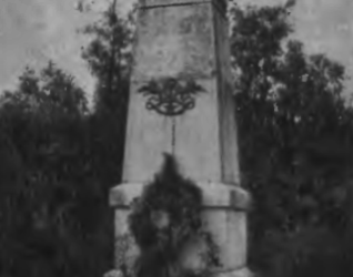 Pomnik generała Bosaka w Burgundii, niedaleko Dijon. Kamienny obelisk z płaskorzeźbami herbów Polski, Litwy i Rusi, otoczony emblematami wojennymi. W tle widoczne drzewa.