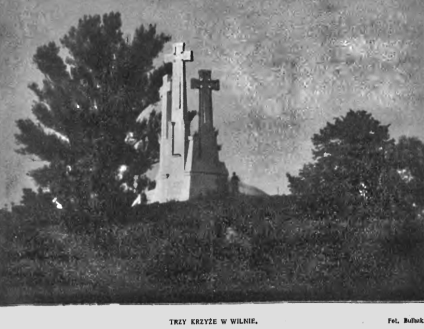 Pomnik trzech krzyży w Wilnie na wzgórzu z drzewami po obu stronach, pod pochmurnym niebem.