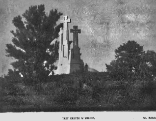 Pomnik trzech krzyży w Wilnie na wzgórzu z drzewami po obu stronach, pod pochmurnym niebem.