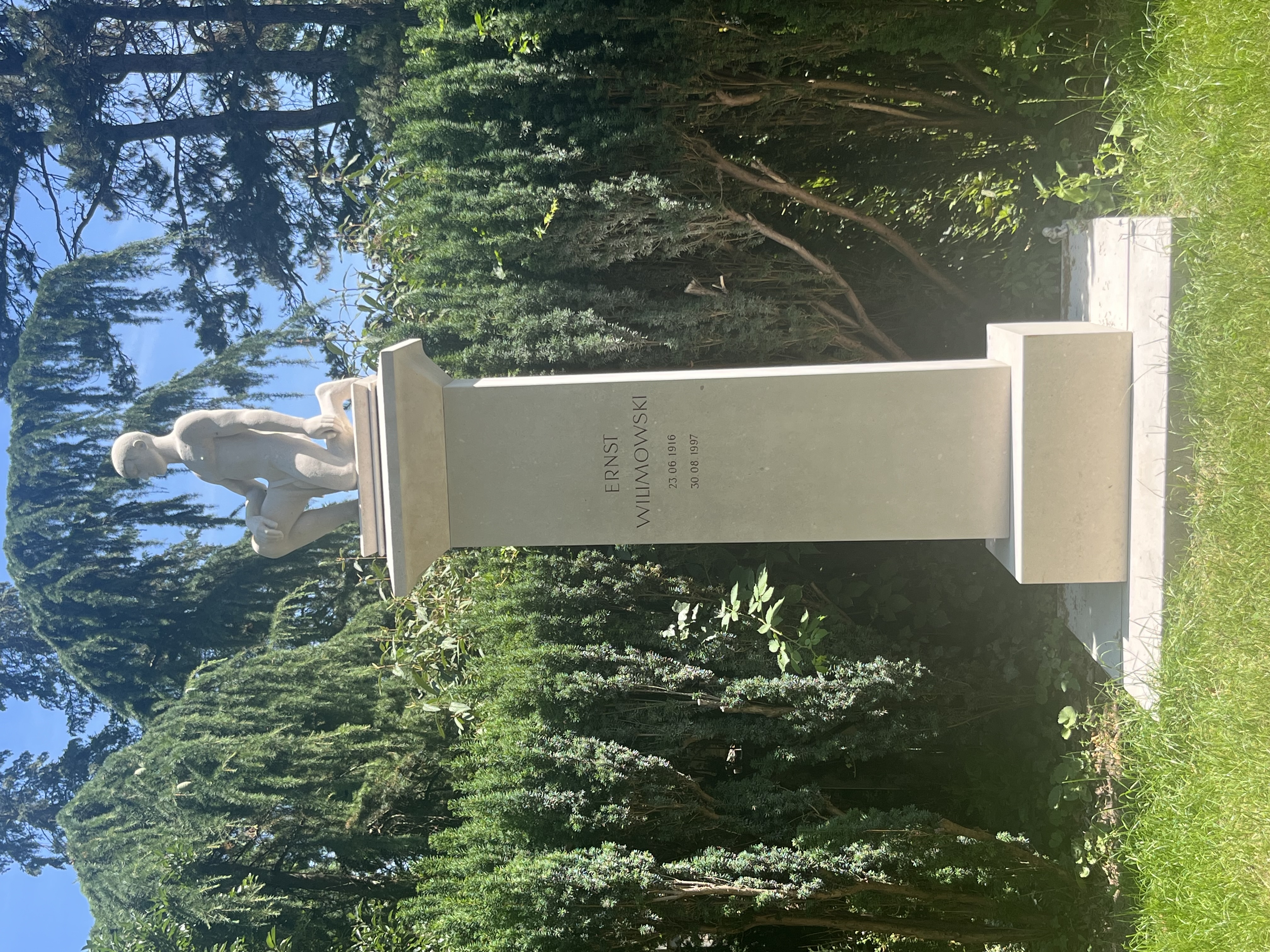 Une simple pierre tombale d'Ernst Wilimowski au Hauptfriedhof de Karlsruhe, avec une sculpture de footballeur et les dates 23.06.1916 - 30.08.1997, entourée de verdure.