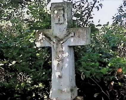 Kamienny krzyż z reliefem Chrystusa na przecięciu ramion, otoczony zielenią. Powyżej znajduje się titulus. Cokół ma ścięte górne krawędzie i jest przykryty węższą płytą.
