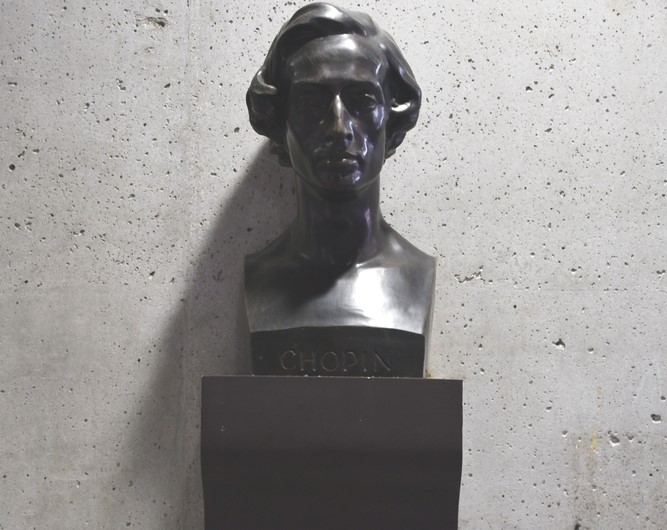 Un buste en bronze de Frédéric Chopin sur un mur de béton dans le passage Chopin à Ljubljana. Le buste présente des traits détaillés et l'inscription "Chopin" sur la base.