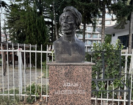 Popiersie Adama Mickiewicza z brązu na granitowym cokole w Strudze, Macedonia Północna, otoczone zielenią.