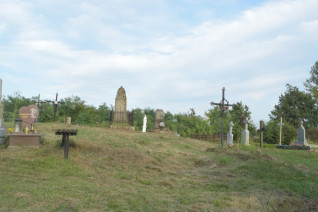 Widok polskiego cmentarza w Krakowcu na Ukrainie, z różnymi nagrobkami i krzyżami na trawiastym terenie pod czystym niebem.