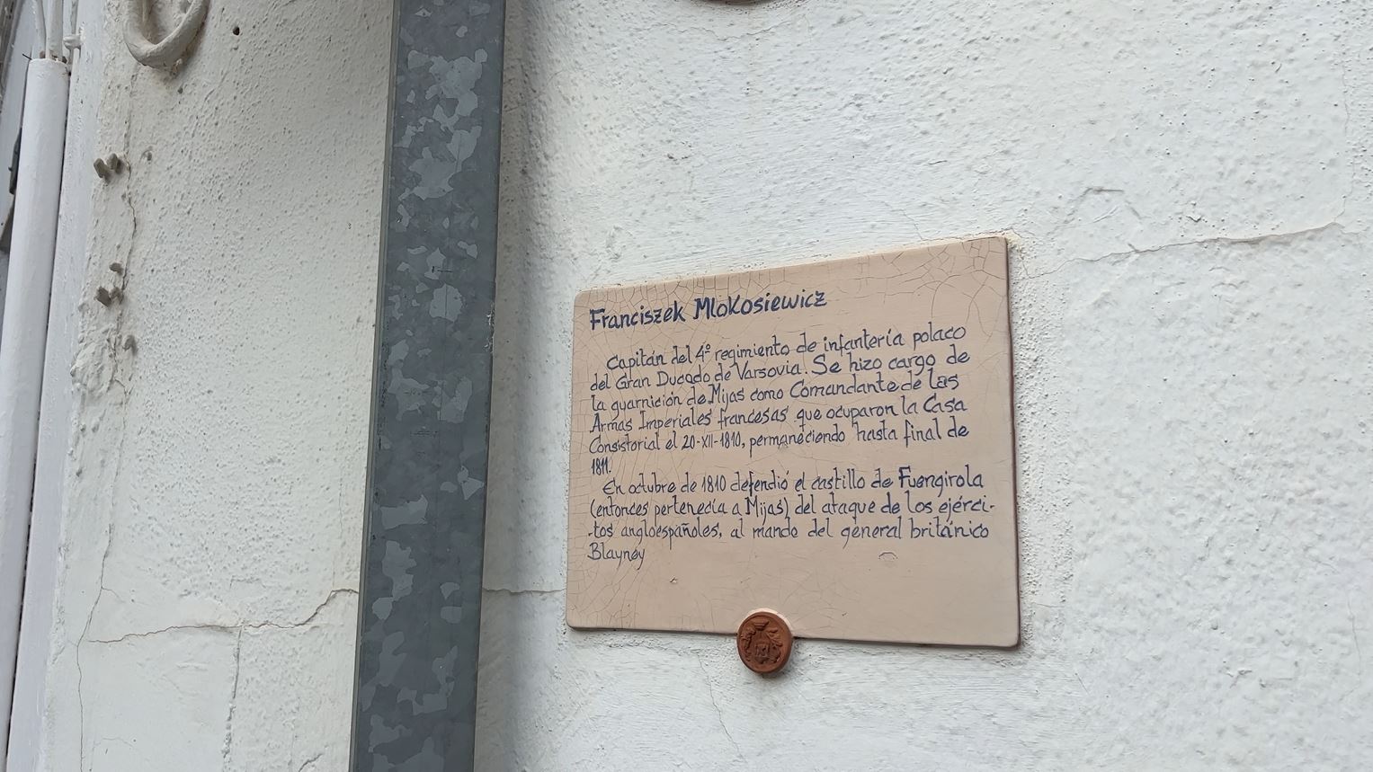 Tablica w Mijas, Hiszpania, upamiętniająca Franciszka Młokosiewicza, polskiego oficera znanego z obrony Fuengiroli w 1810 roku. Tablica zamontowana na białej ścianie z tekstem po hiszpańsku.