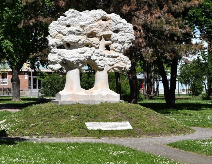 Pomnik Przyjaźni Polsko-Węgierskiej w Győr, przedstawiający dwa splecione dęby, symbolizujące głęboko zakorzenioną relację między Polską a Węgrami. Otoczony zielenią i tablicą z napisami.