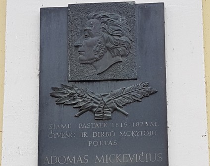 Tablica upamiętniająca Adama Mickiewicza w Kownie, z jego profilem i napisami po litewsku, zamontowana na fasadzie budynku.