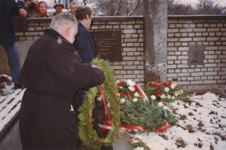 Mężczyzna składa wieniec na grobie żołnierzy polskich poległych we wrześniu 1939 roku. Grób ozdobiony kwiatami, na ceglanej ścianie tablica upamiętniająca poległych żołnierzy.