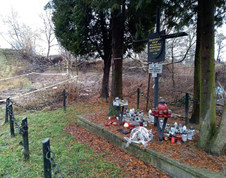 Mogiła zbiorowa żołnierzy polskich z 1939 r. w Hołosku, Lwów. Krzyż z inskrypcjami stoi wśród drzew, otoczony świecami i ogrodzeniem z łańcucha.