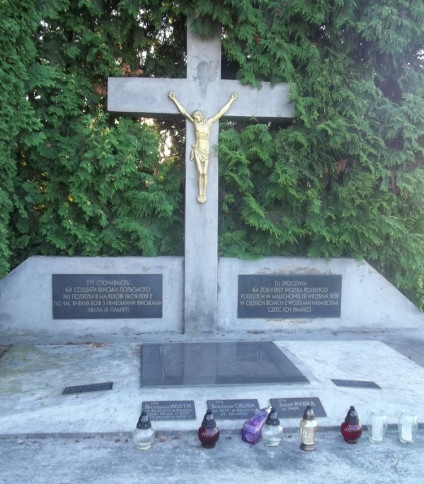 Kamienny krzyż z złotą figurą Chrystusa, otoczony zielenią. Poniżej tablice upamiętniające 64 polskich żołnierzy poległych w Malechowie 19 września 1939 r. Na kamiennej podstawie stoją znicze.