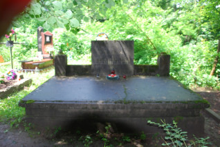 Kamienny sarkofag z pionową płytą inskrypcyjną na cmentarzu, otoczony zielenią. Inskrypcja głosi: 'Bojownikom o niepodległość Polski 1918'.