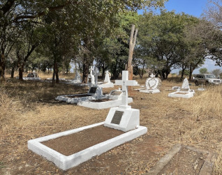 Polska kwatera na cmentarzu w Bwana M'Kubwa, Zambia, z bielonymi grobami i kamieniem z wieńcem laurowym. Wokół znajdują się drzewa i sucha trawa.