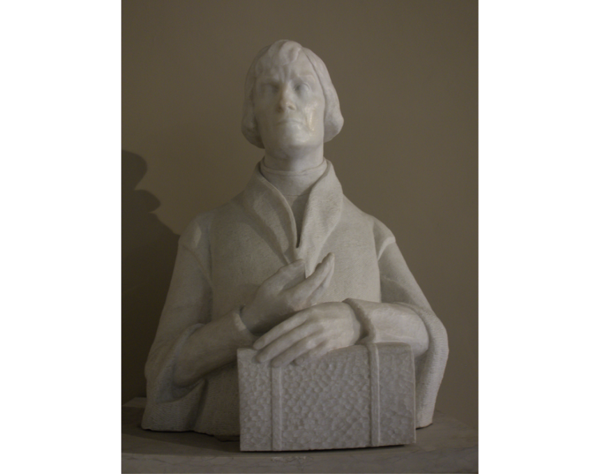 White marble bust of Nicolaus Copernicus, made by Jadwiga Bohdanowicz in 1935. Copernicus rests his left hand on a book and points upwards with his right hand. It is located at the University of Bologna.