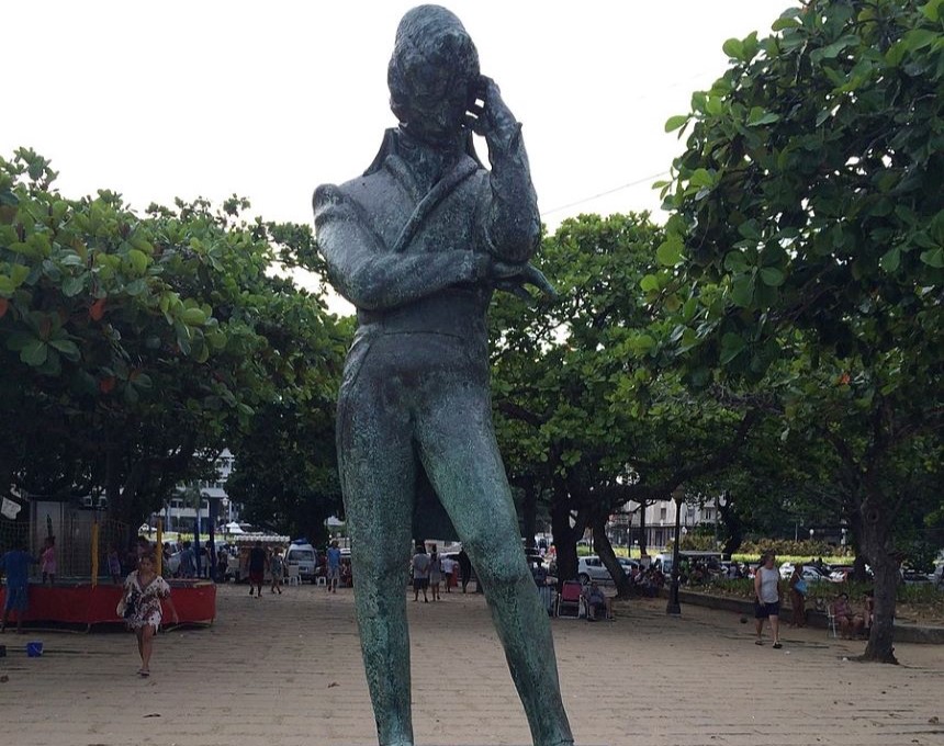Bronze statue of Frédéric Chopin on a low pedestal, surrounded by trees, located on the beach promenade in Rio de Janeiro. The statue depicts Chopin in a pensive pose.
