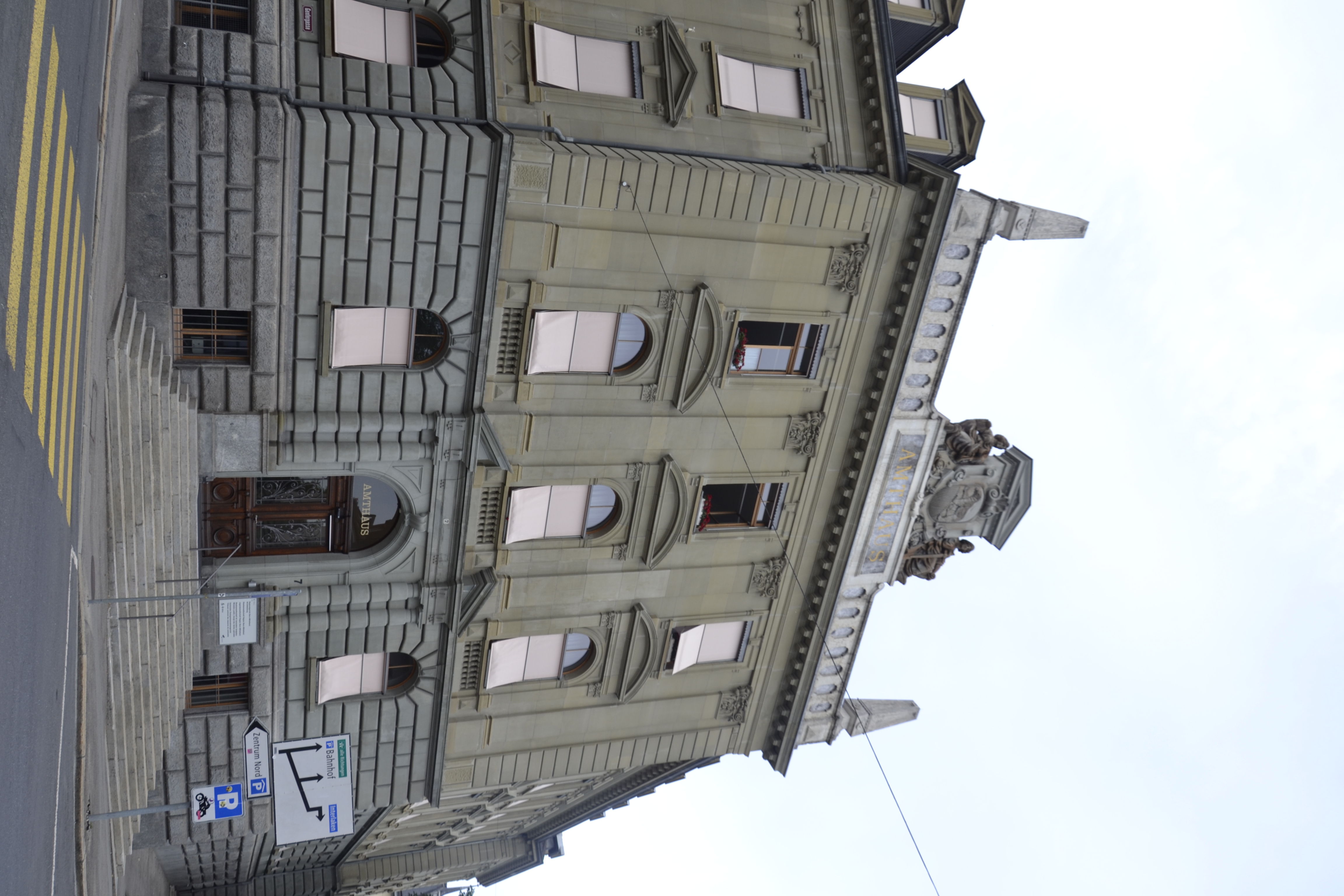 Le bâtiment Amtshaus à Berne, conçu par l'architecte Franciszek Stempkowski, présente une façade néoclassique avec des fenêtres cintrées et des éléments décoratifs. L'entrée est marquée par un escalier menant à une porte en bois.