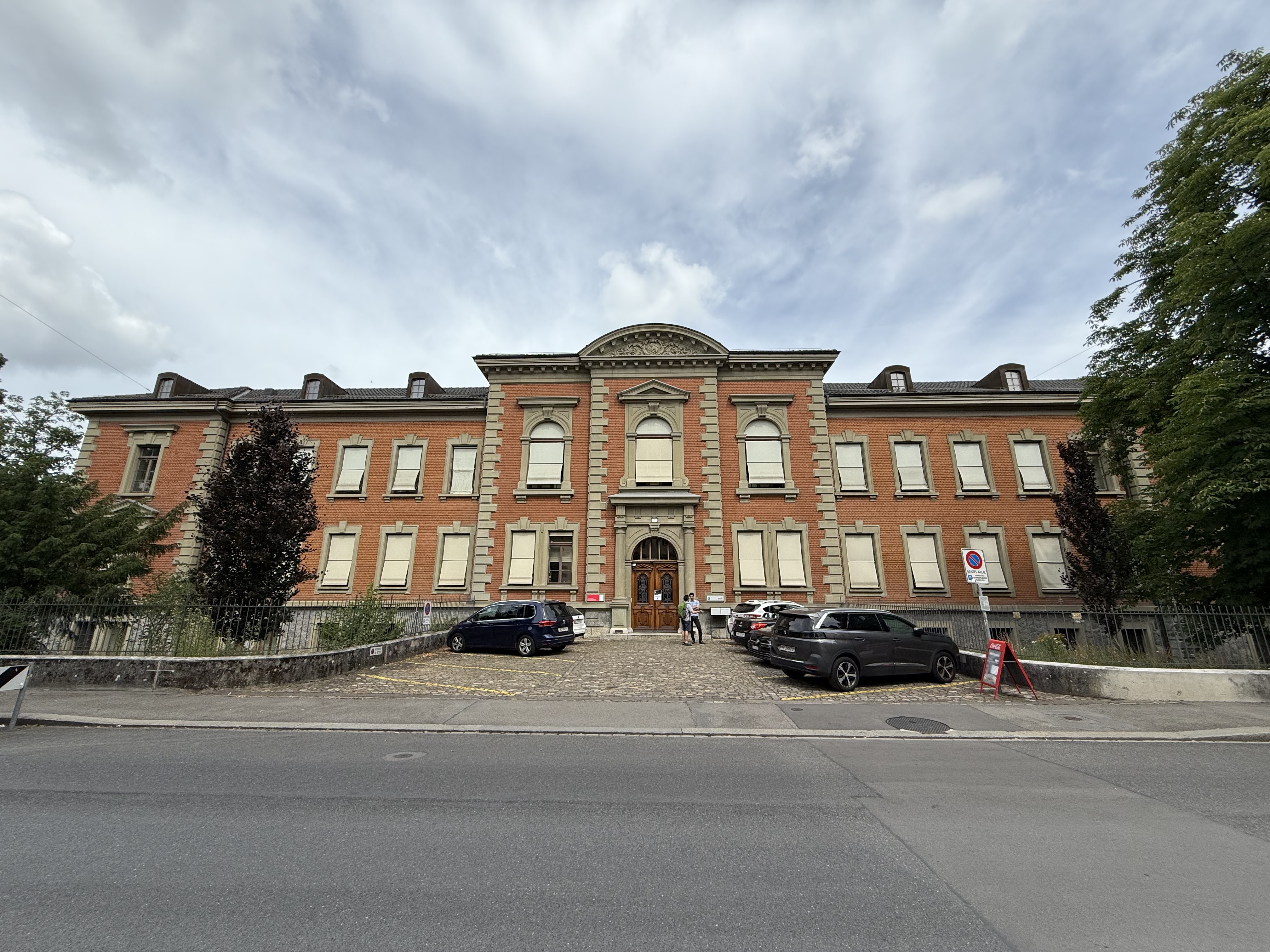 Façade d'un bâtiment en briques rouges avec une entrée centrale, conçu par l'architecte polonais Franciszek Stempkowski à Berne. La structure présente des fenêtres symétriques et un fronton décoratif.