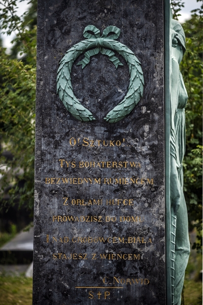 Gravestone of Józef Wieniawski at Ixelles Cemetery in Brussels, featuring a bronze relief of a wreath and an inscription with a quote from Cyprian Norwid's 'Promethidion'.