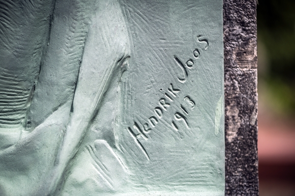 Close-up of a bronze relief on Józef Wieniawski's tombstone at Ixelles Cemetery, showing the signature 'Hendrik Joos 1913' engraved on the surface.