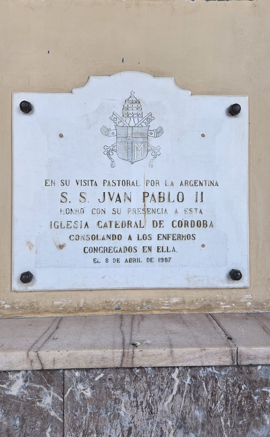 Plaque commémorant la visite de Jean-Paul II à la cathédrale de Córdoba, Argentine, le 8 avril 1987. La plaque comprend les armoiries du pape et un texte en espagnol honorant sa présence.