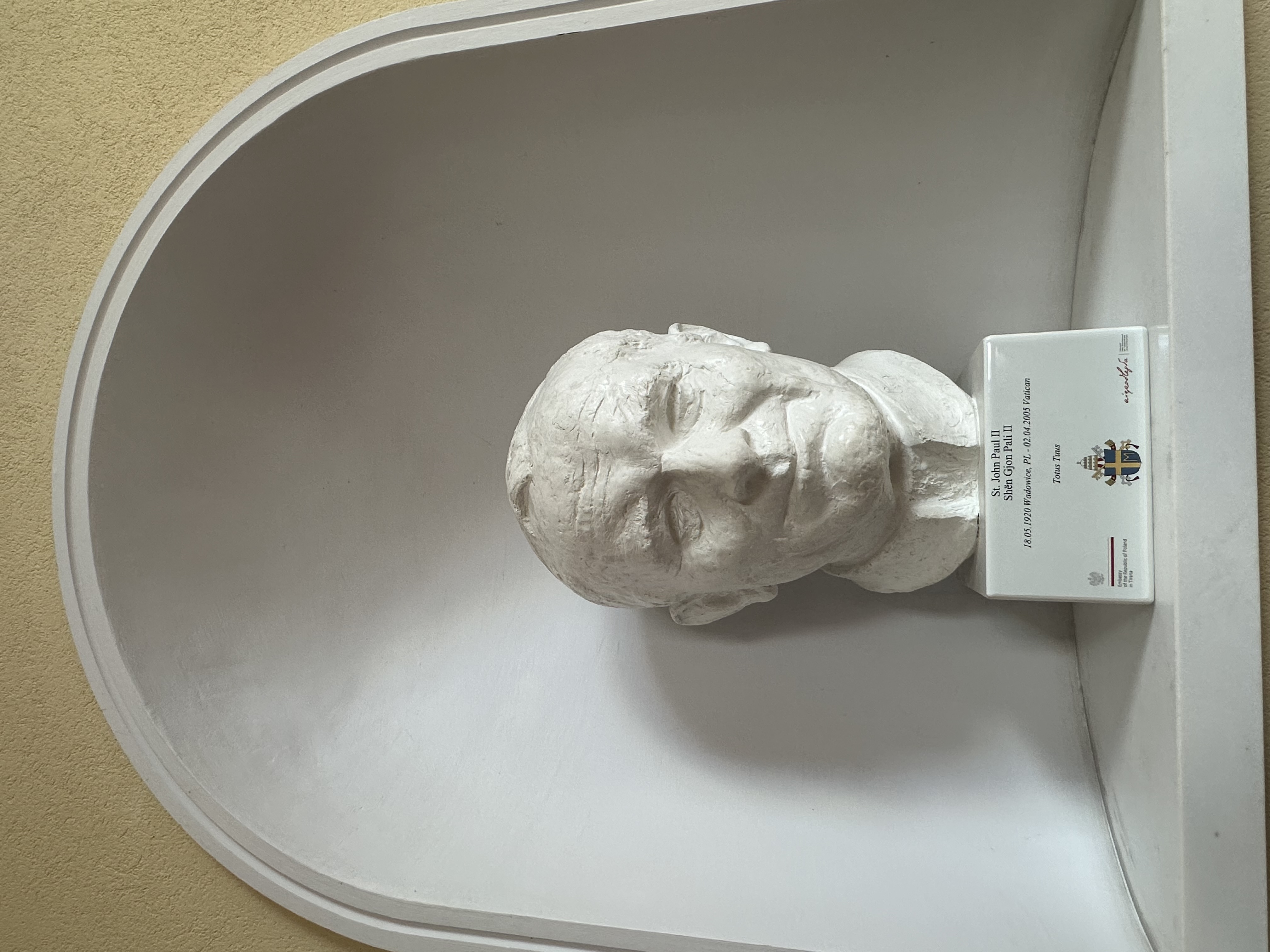 White bust of John Paul II in an alcove with a plaque below. The plaque includes his name, birth and death dates, and the phrase 'Totus Tuus'.