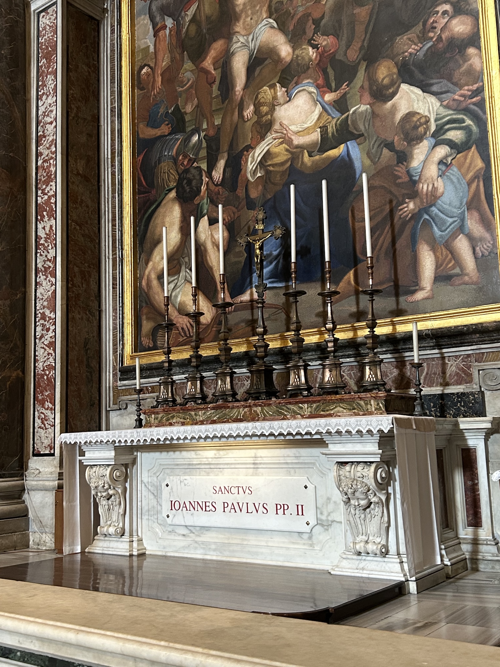Autel en marbre avec l'inscription 'SANCTVS IOANNES PAVLVS PP. II' à l'intérieur d'une église. Au-dessus de l'autel, une grande peinture représente une scène religieuse avec plusieurs personnages. Sept chandeliers sont placés sur l'autel.