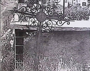 Żeliwny krzyż oznaczający grób Alberta Zdzijowskiego, z ozdobnymi wolutami i tabliczką u podstawy. Krzyż ma spiralne i wolutowe zdobienia, na tle cmentarza.