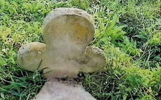 Ułamany krzyż o ramionach zakończonych koliście na pionowej płycie, otoczony trawą. Inskrypcja ryta w dolnej części frontu.
