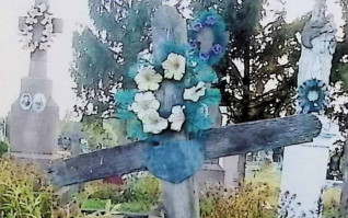 Drewniany krzyż oznaczający grób Karola Barabasza z metalową tabliczką na przecięciu ramion. Tabliczka ma kształt kartusza z wyrytą inskrypcją.