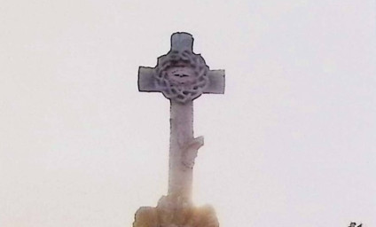 Krzyż stylizowany na pień drzewa z koroną cierniową na przecięciu ramion, na cokole w formie stosu kamieni.