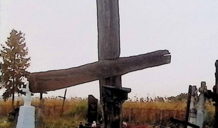 Drewniany krzyż oznaczający grób Zofii Siusadz z przełamaną metalową tabliczką w formie rozwiniętego zwoju na przecięciu ramion.