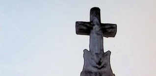 Nagrobek z krzyżem stylizowanym na pień drzewa, z postacią Chrystusa na przecięciu ramion. U podstawy wieniec z liści. Cokół przypomina stos kamieni z inskrypcją na zwoju.