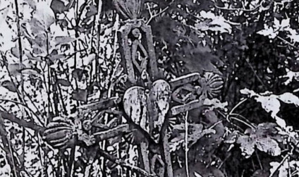 Żeliwny krzyż na cokole z ramionami zakończonymi palmetami i tablicą w kształcie serca na przecięciu. Krzyż zdobiony rombami i esownicami, otoczony roślinnością.