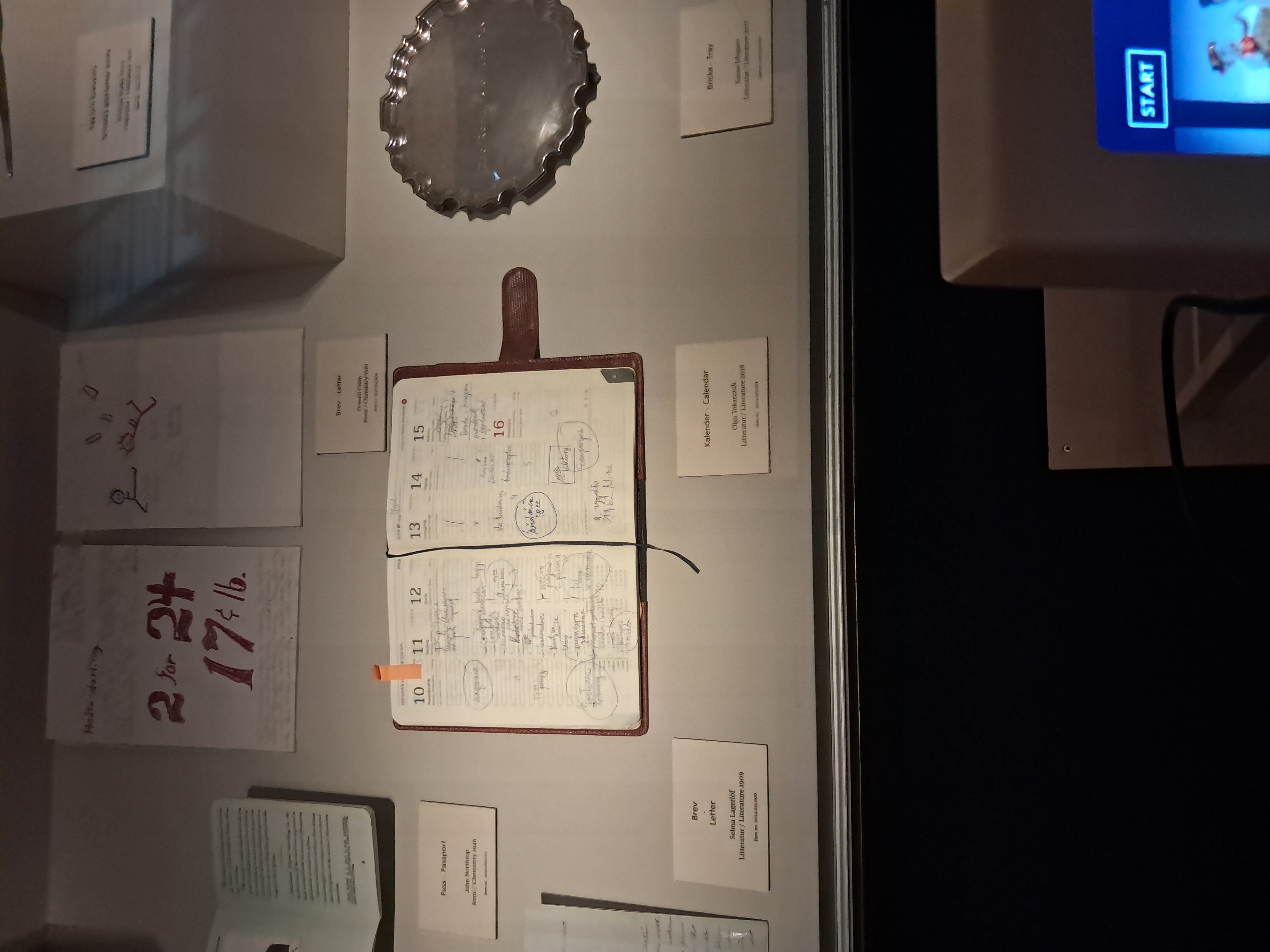 Vitrine au Musée Nobel à Stockholm avec le calendrier d'Olga Tokarczuk, un plateau en argent et divers documents liés aux lauréats du Nobel.