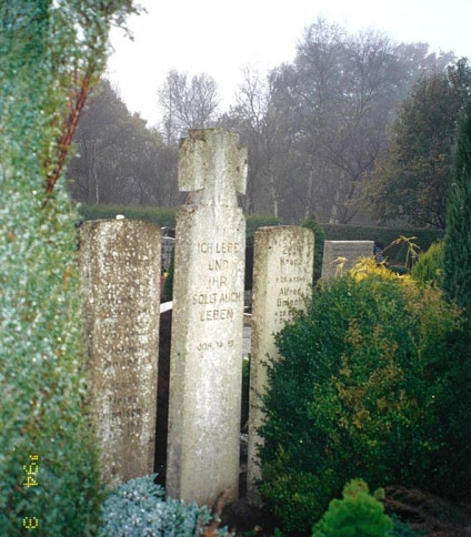 Nagrobki na cmentarzu w Langholt, w tym centralna tablica z piaskowca z krzyżem Wehrmachtu i cytatem z Jana 14:19. Otaczająca zieleń i drzewa w tle.