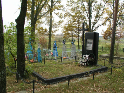 Grób Polaków zamordowanych przez Ukraińską Powstańczą Armię w 1943 roku, znajdujący się na cmentarzu z drzewami i czarnym pomnikiem z inskrypcjami. Wokół umieszczone są wieńce i kwiaty.