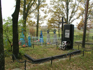 Grób Polaków zamordowanych przez Ukraińską Powstańczą Armię w 1943 roku, znajdujący się na cmentarzu z drzewami i czarnym pomnikiem z inskrypcjami. Wokół umieszczone są wieńce i kwiaty.