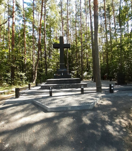 Duży czarny krzyż otoczony drzewami, upamiętniający polskie ofiary Ukraińskiej Powstańczej Armii w Janowej Dolinie.
