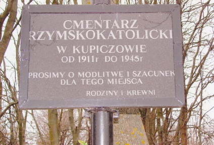 Tabliczka na krzyżu na cmentarzu rzymskokatolickim w Kupiczowie z napisem: 'Cmentarz / rzymskokatolicki / w Kupiczowie / od 1911 r. do 1945 r. / Prosimy o modlitwę i szacunek / dla tego miejsca / Rodziny i krewni'.