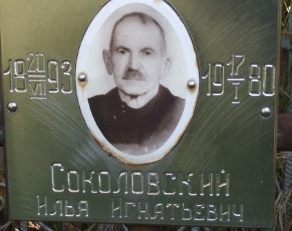 Metalowa tabliczka z fotografią mężczyzny i rosyjskim napisem. Widoczne daty 1893 i 1980. Tabliczka jest częścią grobu na cmentarzu rodziny Sokołowskich.