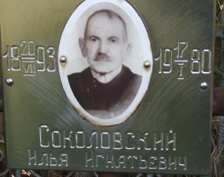 Metalowa tabliczka z fotografią mężczyzny i rosyjskim napisem. Widoczne daty 1893 i 1980. Tabliczka jest częścią grobu na cmentarzu rodziny Sokołowskich.