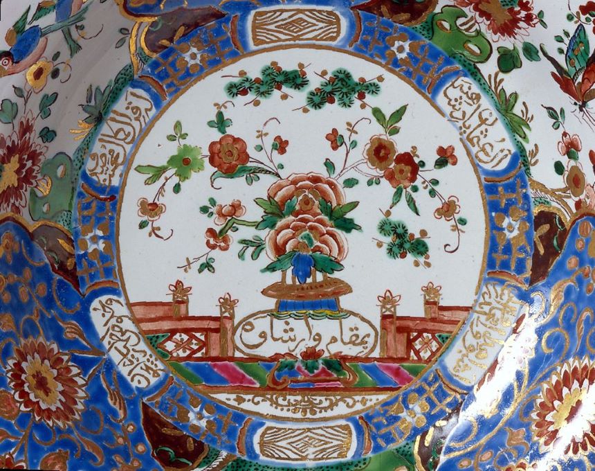 Gros plan sur une assiette du service du sultan de la Manufacture royale de faïence de Belweder, avec un bouquet floral au centre, entouré d'une écriture coufique et de décorations complexes en bleu, rouge et or.